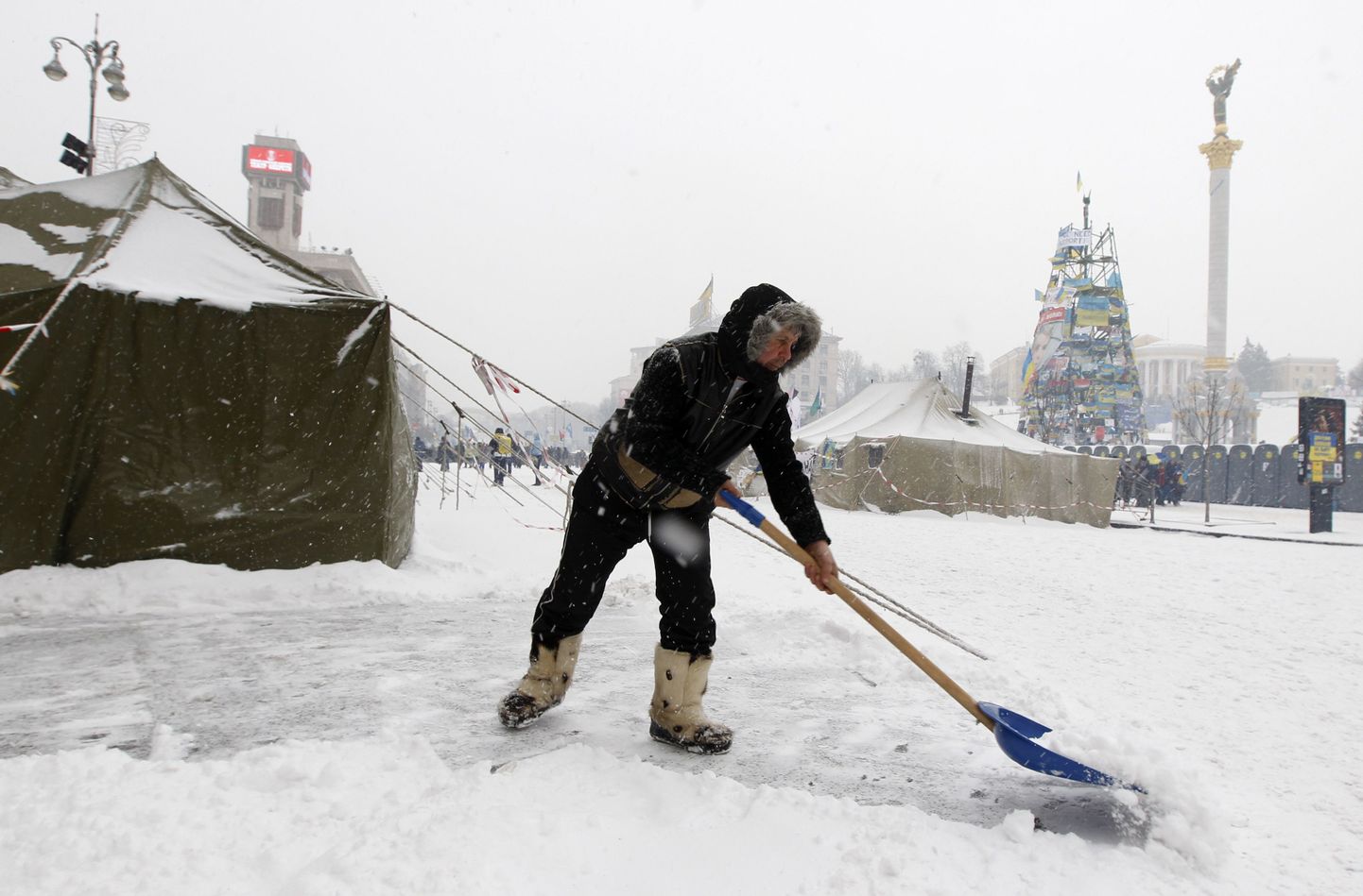 Mees roogib Kiievis Iseseisvuse väljakul lund. Eemal paistavad Maidani sissepiiranud siseväelased.