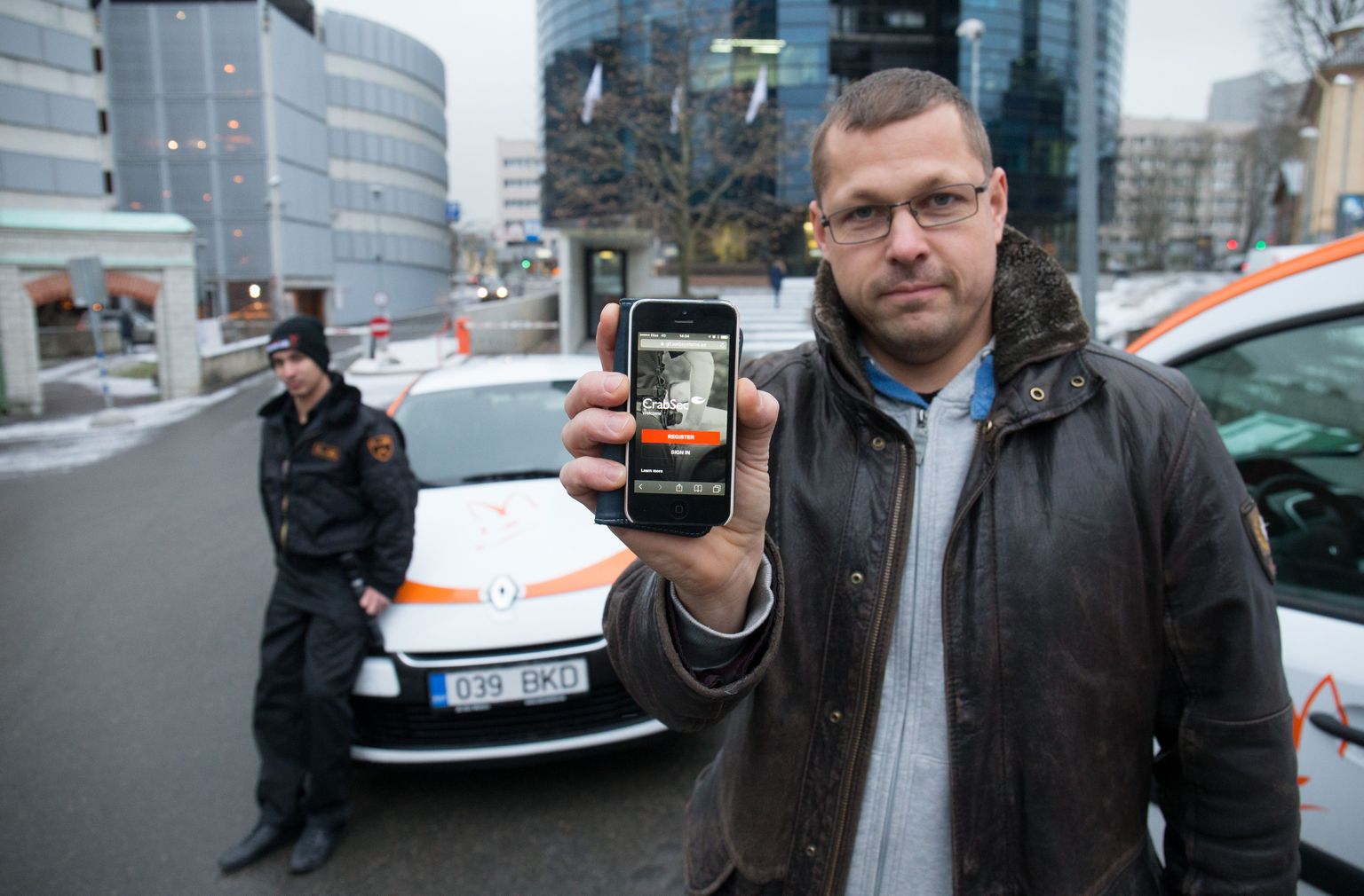 CrabSeci looja Tarmo Pruuli näitamas enda loodud turvarakendust. Uue äpi kasutamist alustas esimesena väike turvafirma Fennec Lis, kelle patrullmeeskonna liige Aleksander Kotilevski toetub tagaplaanil auto kapotile.
