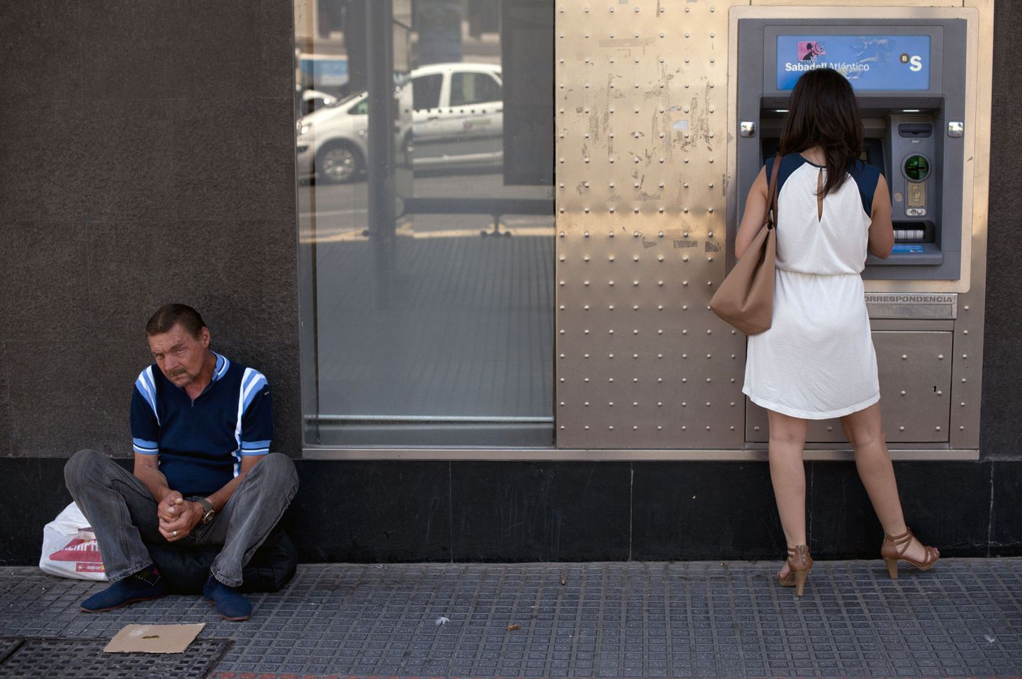 Mees kerjab Malagas, Hispaanias, samal ajal kui naine võtab automaadist raha välja.