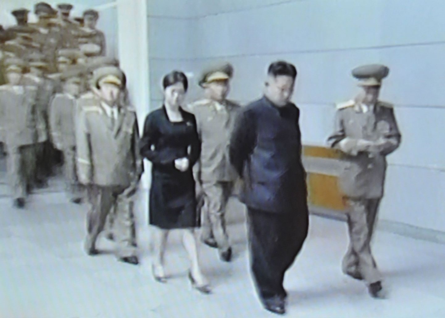 Kaader Põhja-Korea televisioonis näidatud saatest. Pildil selle riigi juht Kim Jong-un koos teda saatnud naissoost isiku ja sõjaväelastega