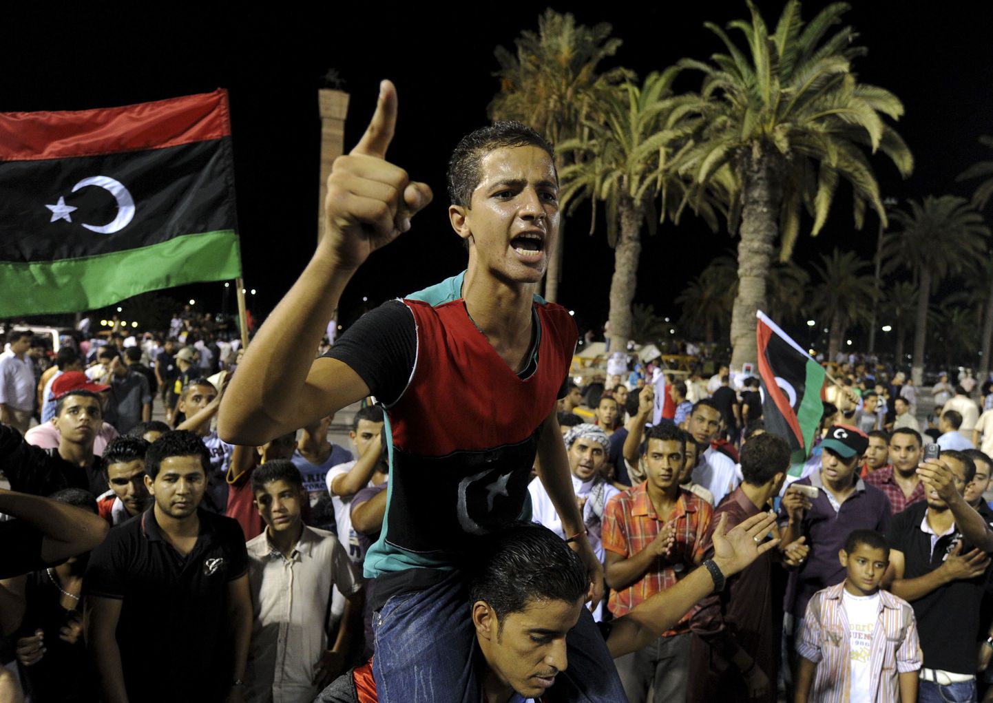 Liibüa noored eile Tripolis Märtrite väljakul uue riigilipu taustal.