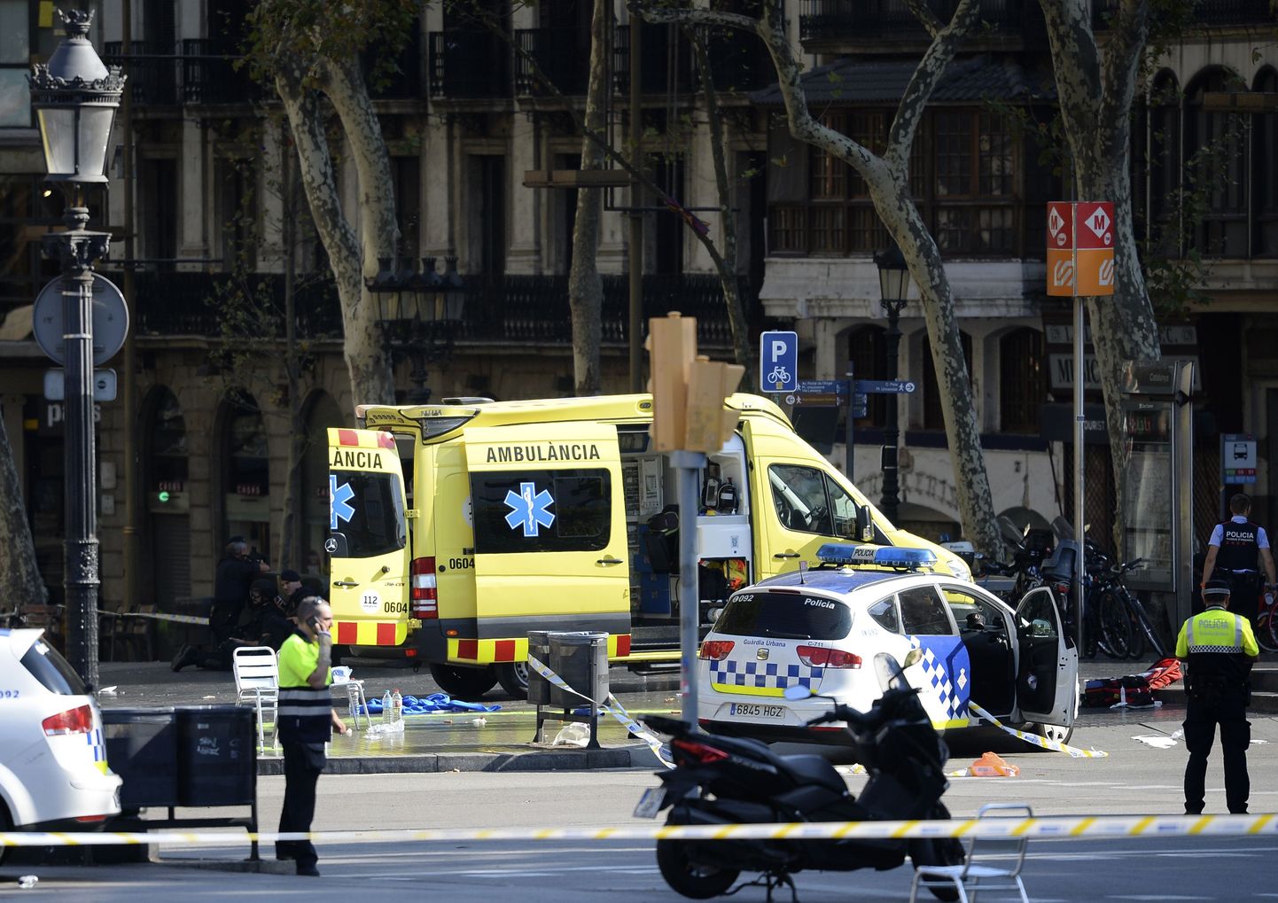A policemen and a medical staff member stand past police cars and an ambulance in a cordoned off area after a van ploughed into the crowd, injuring several persons on the Rambla in Barcelona on August 17, 2017. / AFP PHOTO / Josep LAGO