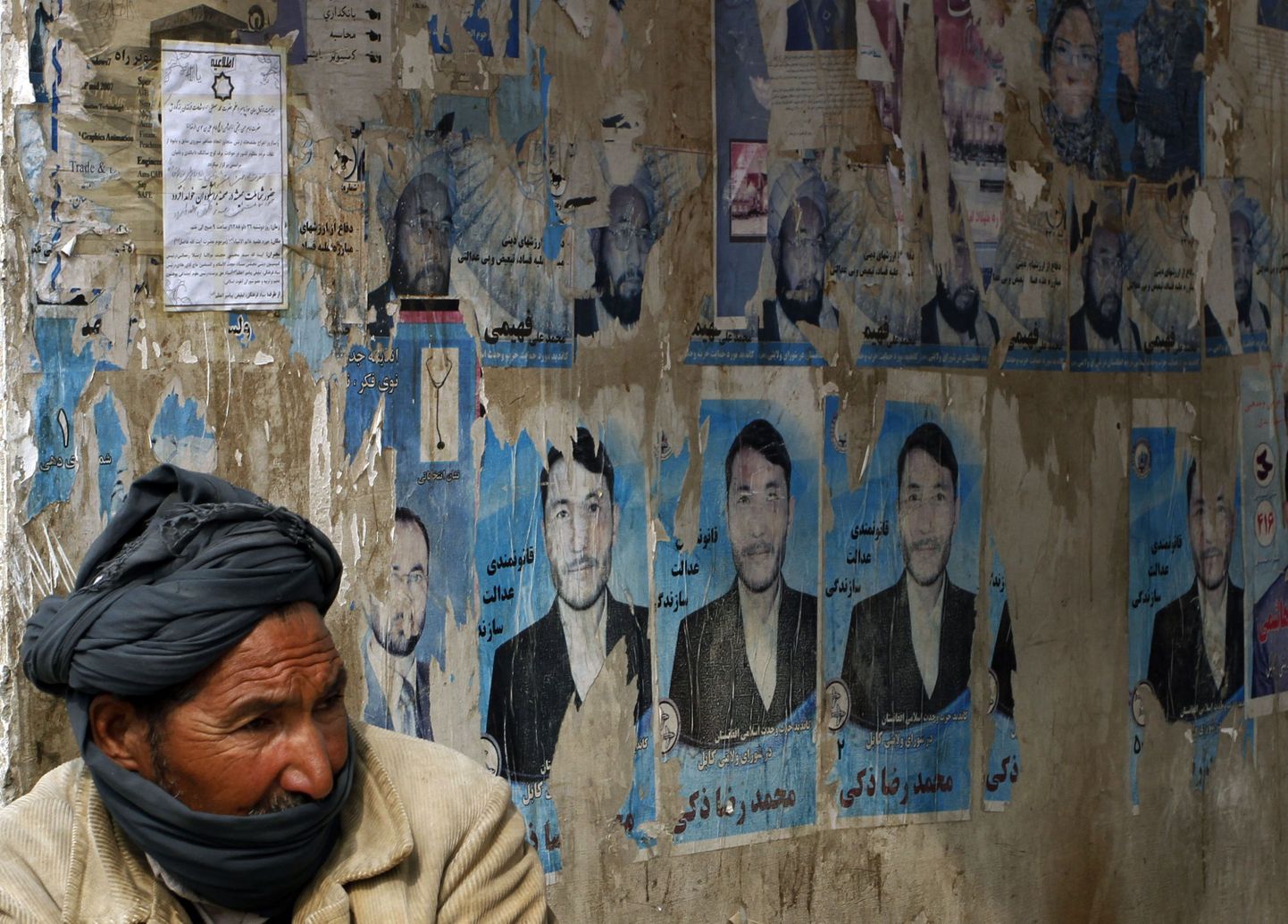 Afgaani mees istumas presidendikandidaatide plakatite taustal.