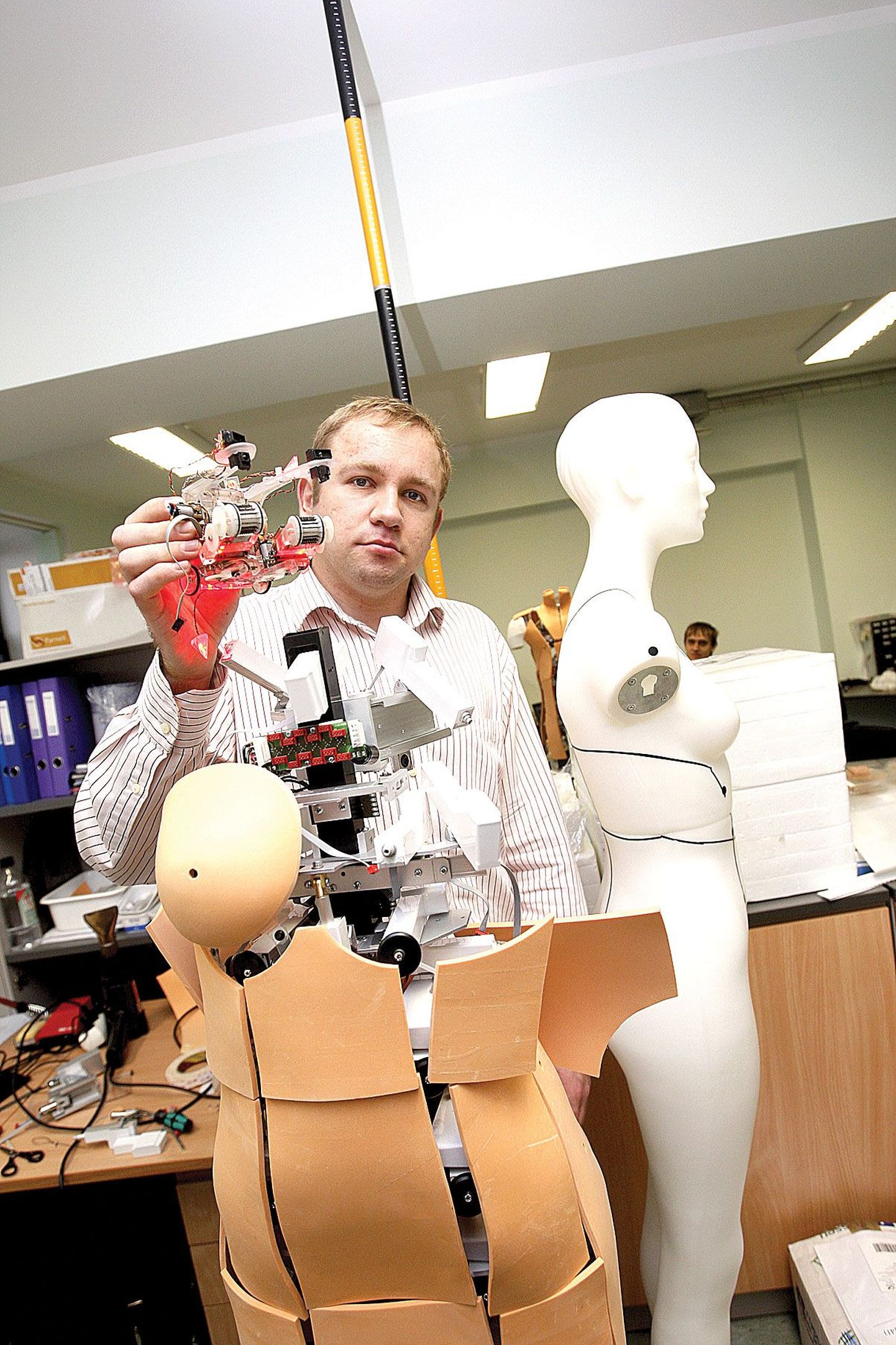 Tartu Ülikooli ettevõtlussuhete koordinaator Vahur Valdna hoiab tudengite ehitatud robotit, mis suudab köit pidi üles ronida. Tema ees seisvad robotmannekeenid on tema sõnul hea näide ettevõtluses kasutatavatest robotitest.