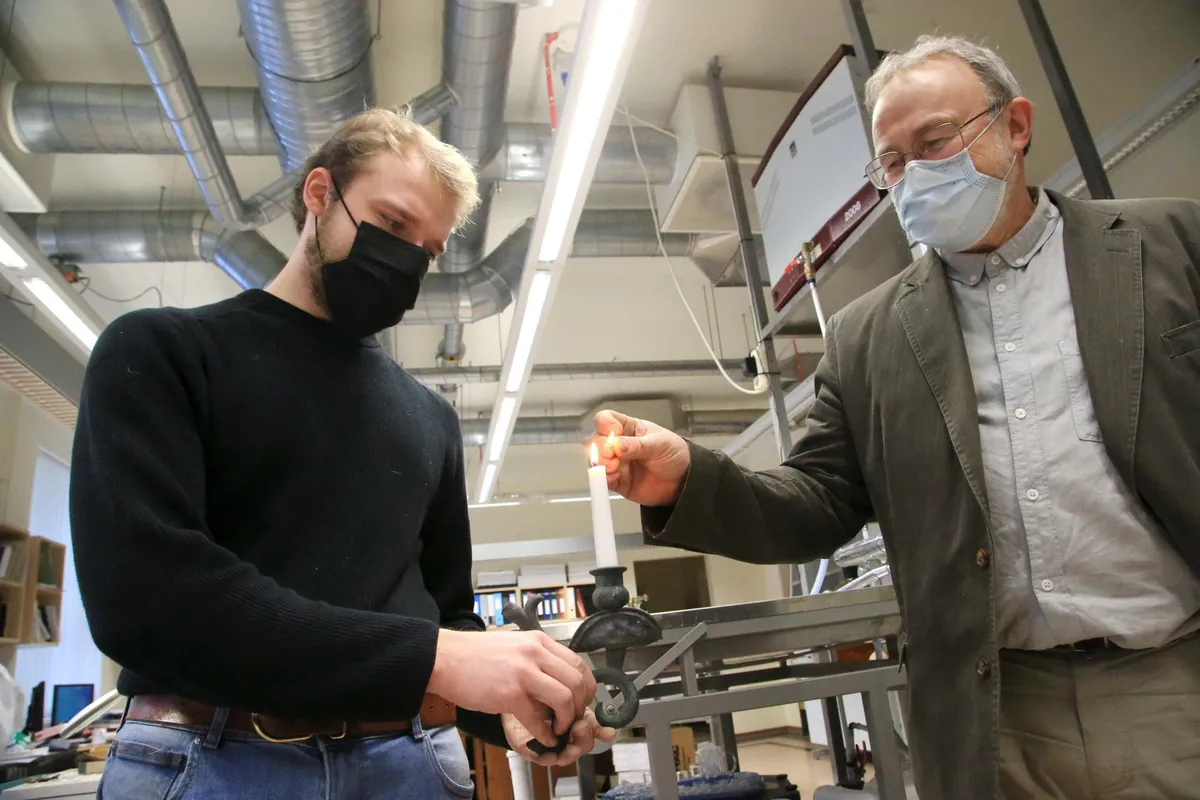 Tartu ülikooli arheoloogiatudeng Mait Raudsepp (vasakul) ja arheoloogiaprofessor Heiki Valk süütavad küünla Karula kiriku lühtri tükil.