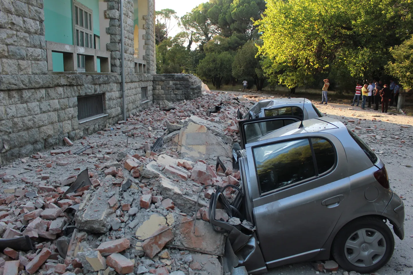 epa07859750 Locals stand at a safe area to watch the damages of crushed cars next to a building of the University of Geology and Mine, after a 5.8 magnitude earthquake hit in Tirana, Albania, 21 September 2019. According to reports, Albania was rocked by its strongest earthquake in 30 years, with the epicentre in the coastal town of Durres, at least 49 people have been reported injured from the earthquake.  EPA/MALTON DIBRA
