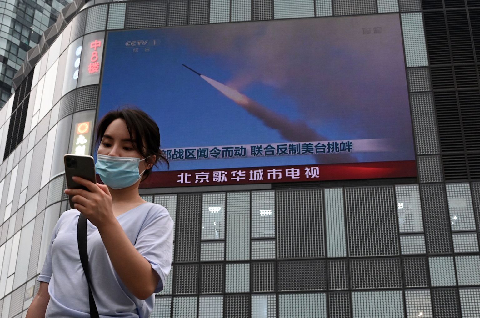 Naine Pekingis Taiwani saare läheduses peetavaid militaarõppuseid näitava ekraani ees.