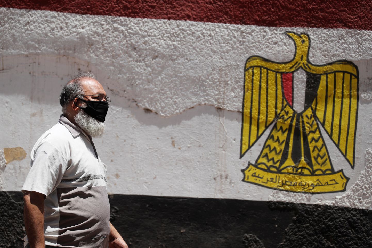 Näomaskis mees Egiptuse lipuvärvidesse maalitud seina kõrval.