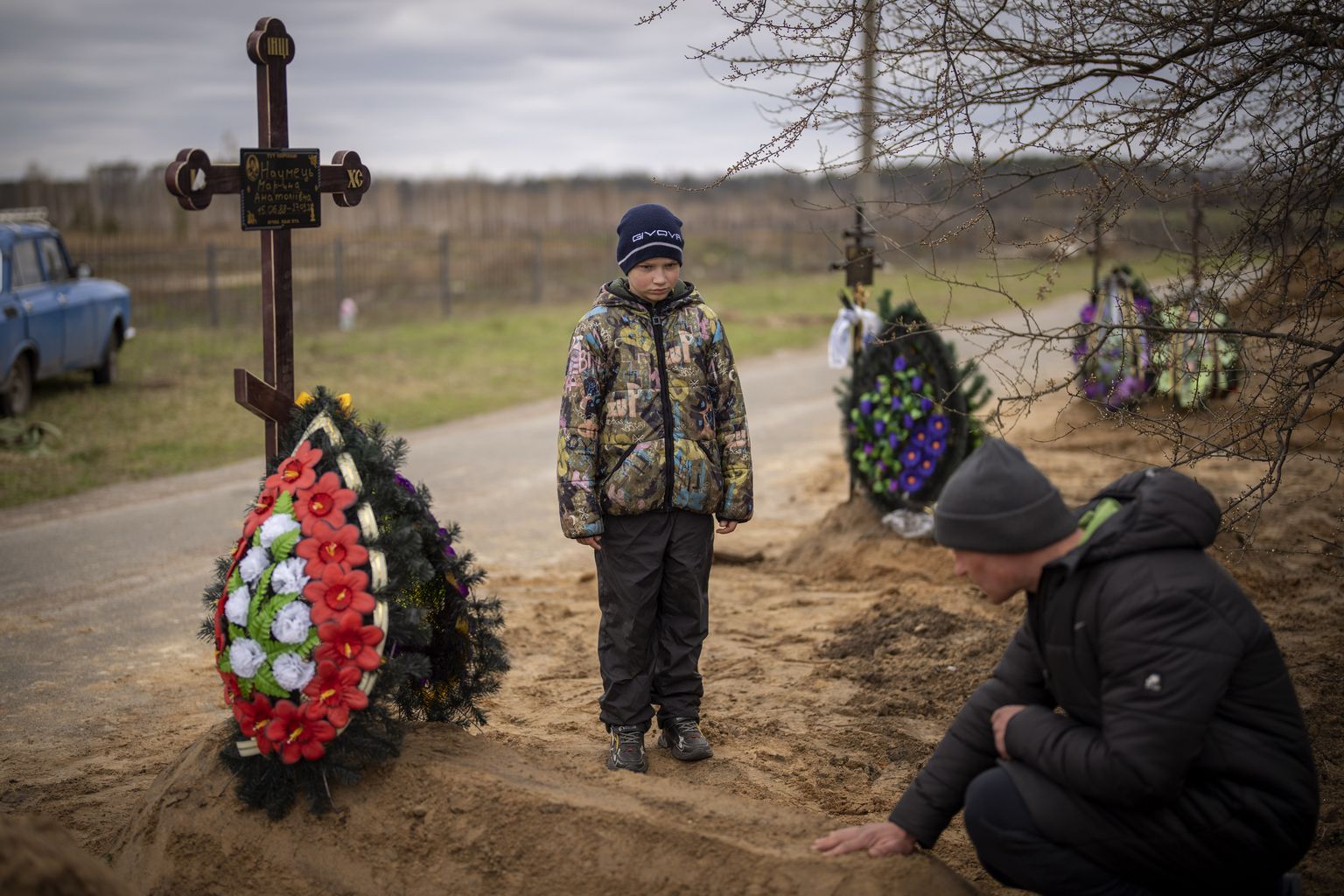 10-летний Вова смотрит на могилу своей матери Марины, пока его отец, Иван Драгун, молится во время ее похорон в Буче, на окраине Киева, Украина, 20 апреля 2022 года. Мать Вовы умерла, когда они укрывались в холодном подвале более месяца во время российской военной оккупации.