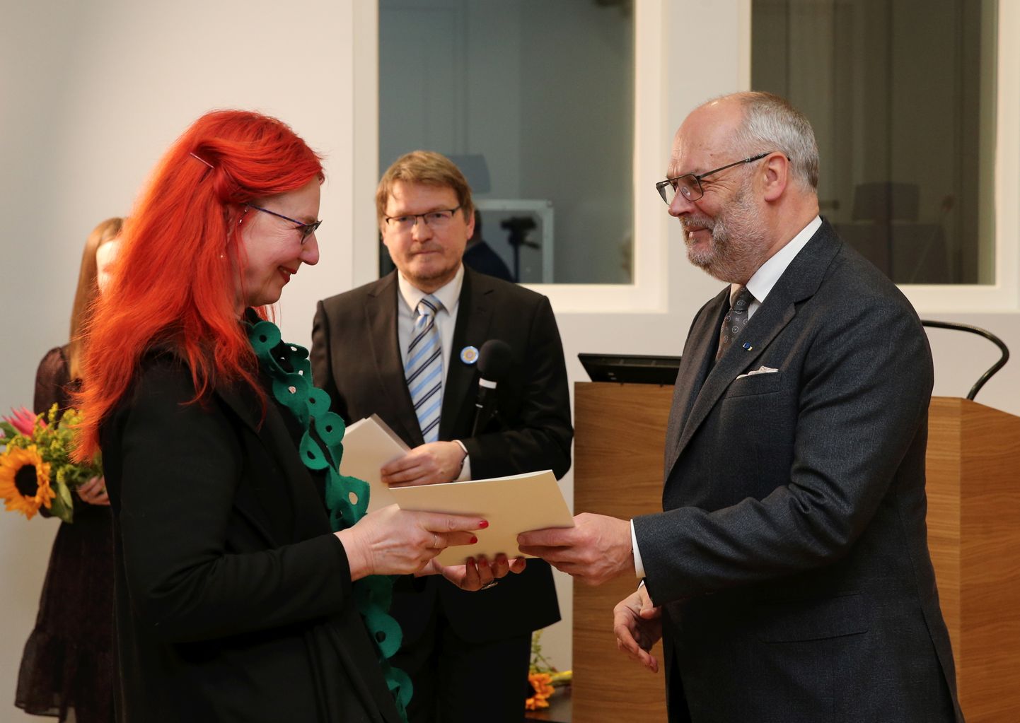 President Alar Karis õnnitleb Eve Kaske rahvaluulearhiivi juhataja Risto Järve silma all.