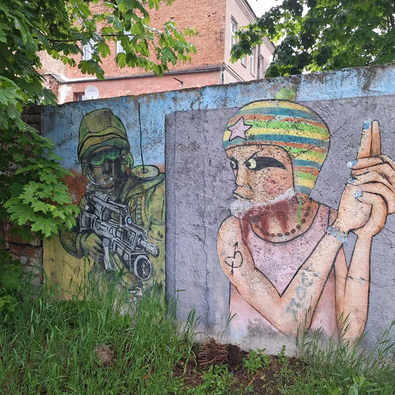 Граффити на стене в заросшем кустарником дворе среди домов в центре Даугавпилса.