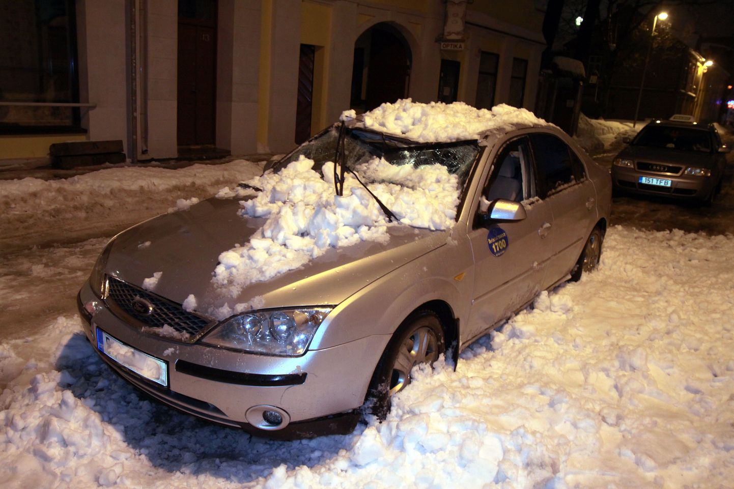 Pärnus Hommiku tänaval lumevaringu alla jäänud auto.