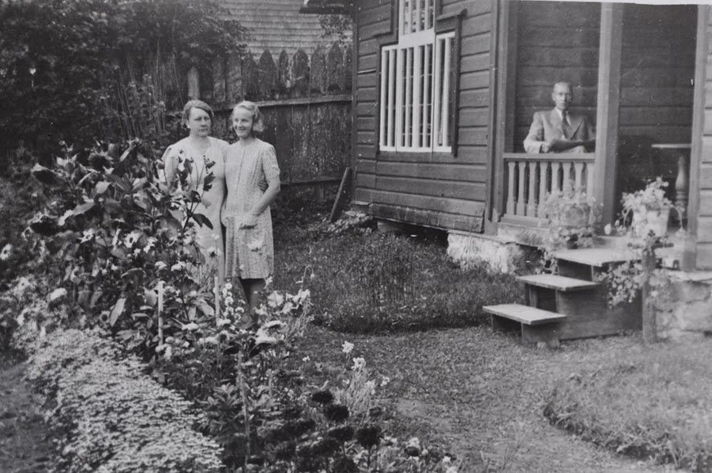 Paide päevapiltnik Jaan Eelnurme oma koduaias Rüütli tänavas. Lillede juures on koha sisse võtnud ka abikaasa Anna ja tütar Heljo. Foto on tehtud 1943. aastal. Sõjategevuse tõttu oli Jaanil sel ajal tööd vähem ja tervise halvenemise tõttu hakkas ta oma pikaajalise ja eduka piltnikukarjääri otsi vaikselt koomale tõmbama. 1943