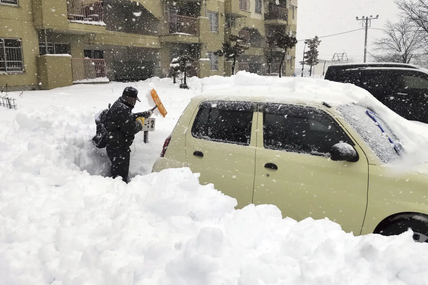 Житель сгребает снег с машины на парковке в городе Китами, префектура Хоккайдо.