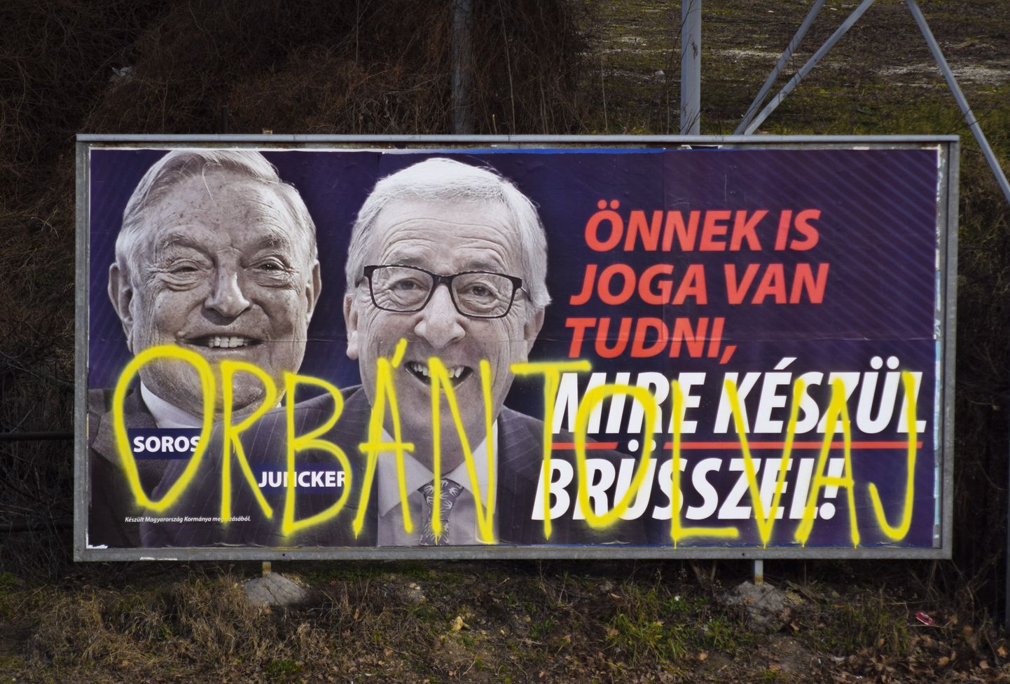 Fotol on plakat Ungari peaministri Viktor Orbáni juhitud valitsuse kampaaniast. Plakatil on näha Euroopa Komisjoni president Jean-Claude Juncker ja Ungari-USA topeltkodakondne George Soros koos kirjaga "Ka sinul on õigus teada, mida Brüssel tegema valmistub". Tekstile on kollase värviga peale kritseldatud lause "Varas Orbán", millega viidatakse arvamusele, et Orbán ja tema lähikond on üks Ungaris leviva korruptsiooni allikatest.