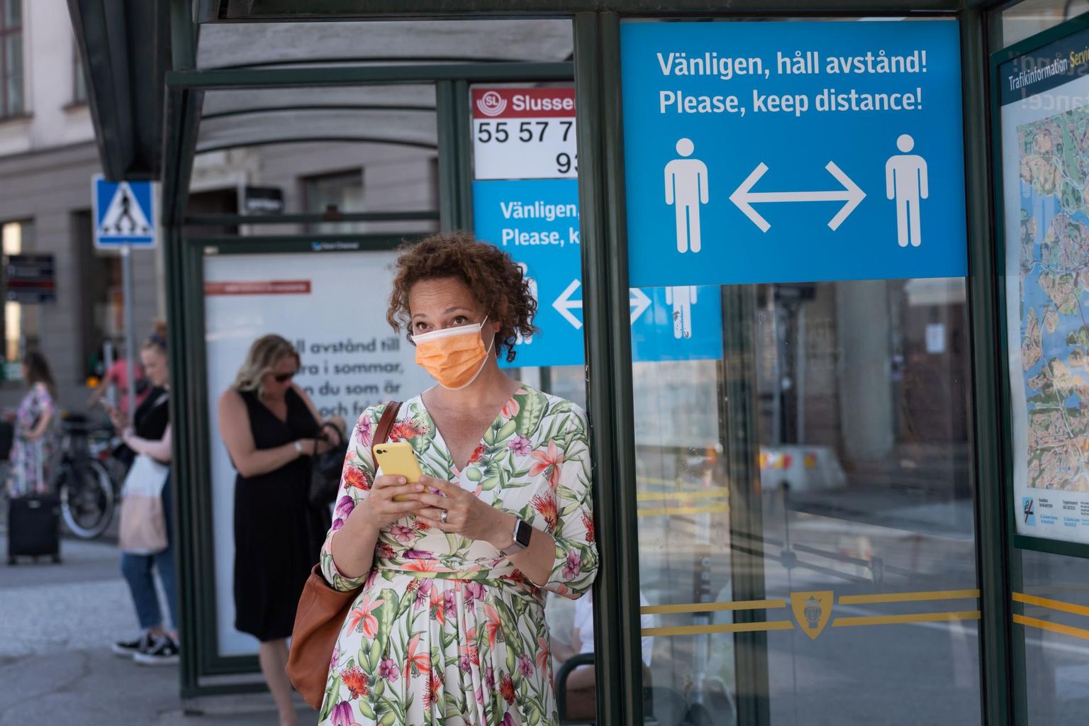 Näomaskiga naine Rootsi pealinnas Stockholmis bussipeatuses, millel olev kiri palub inimestel hoida üksteisega distantsi. 