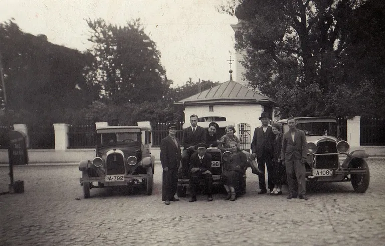 See foto on tehtud 1930. aastate esimesel poolel Tallinnas praeguse Liivalaia tänava ääres Kaasani kiriku juures asunud seisu­platsil, kus taksojuhid ootasid kliente. Auto iluvõrel on Rooma number II, mis tähistab autode kuulumist teise liiki. Teine liik tähendas, et autod olid väiksemad ja vähem võimsad kui esimese klassi omad ning seetõttu ka kliendile odavamad.