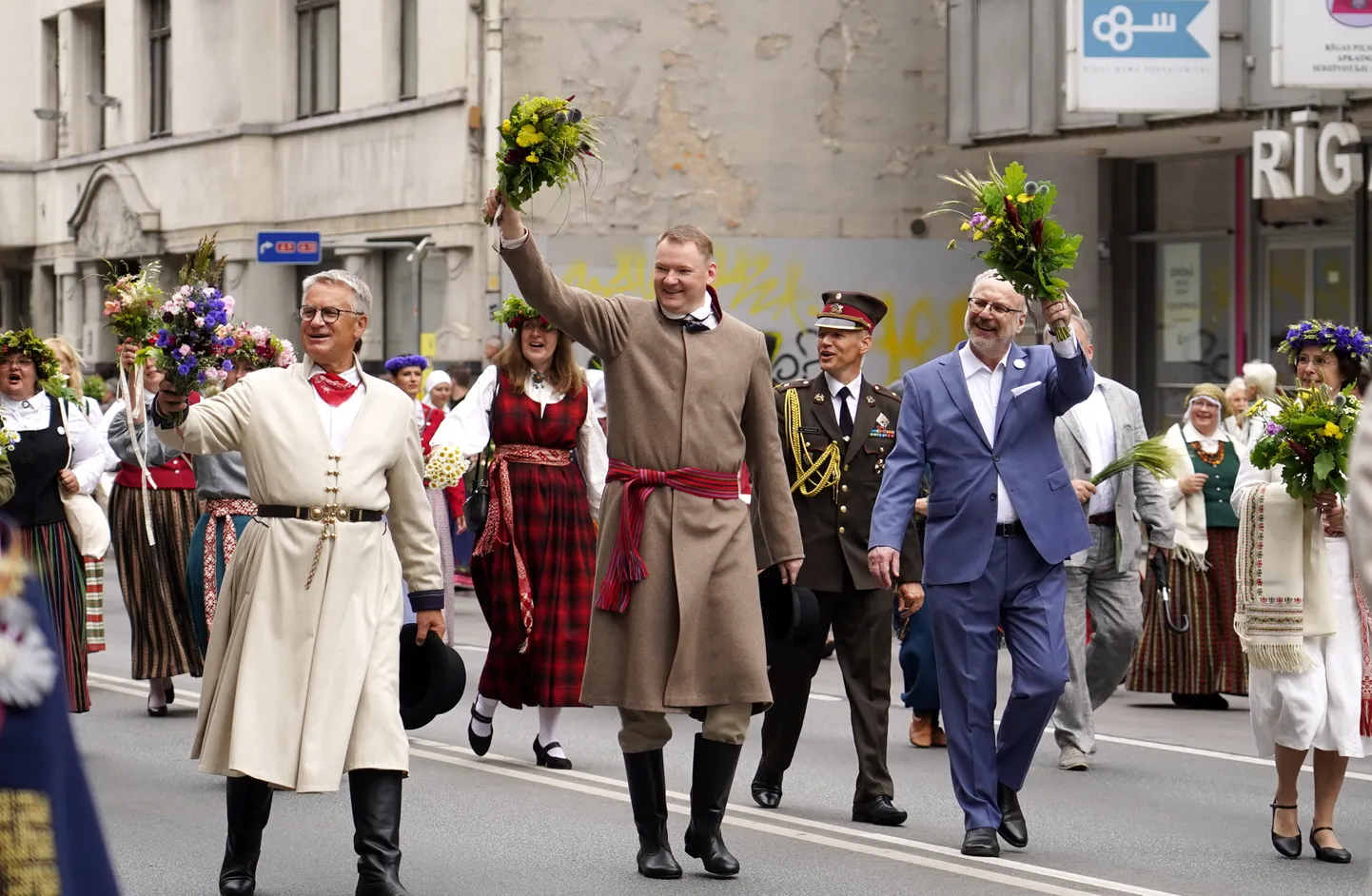Kultūras ministrs Nauris Puntulis, Saeimas priekšsēdētājs Edvards Smiltēns, Valsts prezidents Egils Levits un Valsts prezidenta kundze Andra Levite XXVII Vispārējo latviešu Dziesmu un XVII Deju svētku dalībnieku gājienā "Novadu dižošanās".