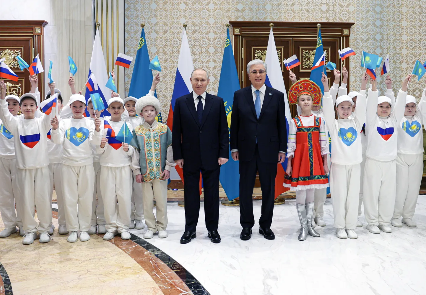 Kasahstani president Kassõm Žomart Tokajev ja Venemaa režiimi juht Vladimir Putin 27. novembril 2024 Astanas koos koolilastega, kes just-just deklameerisid agressorile ja Ukraina vastu toime pandud sõjakuritegude peasüüdlasele luuletust rahvaste sõprusest.