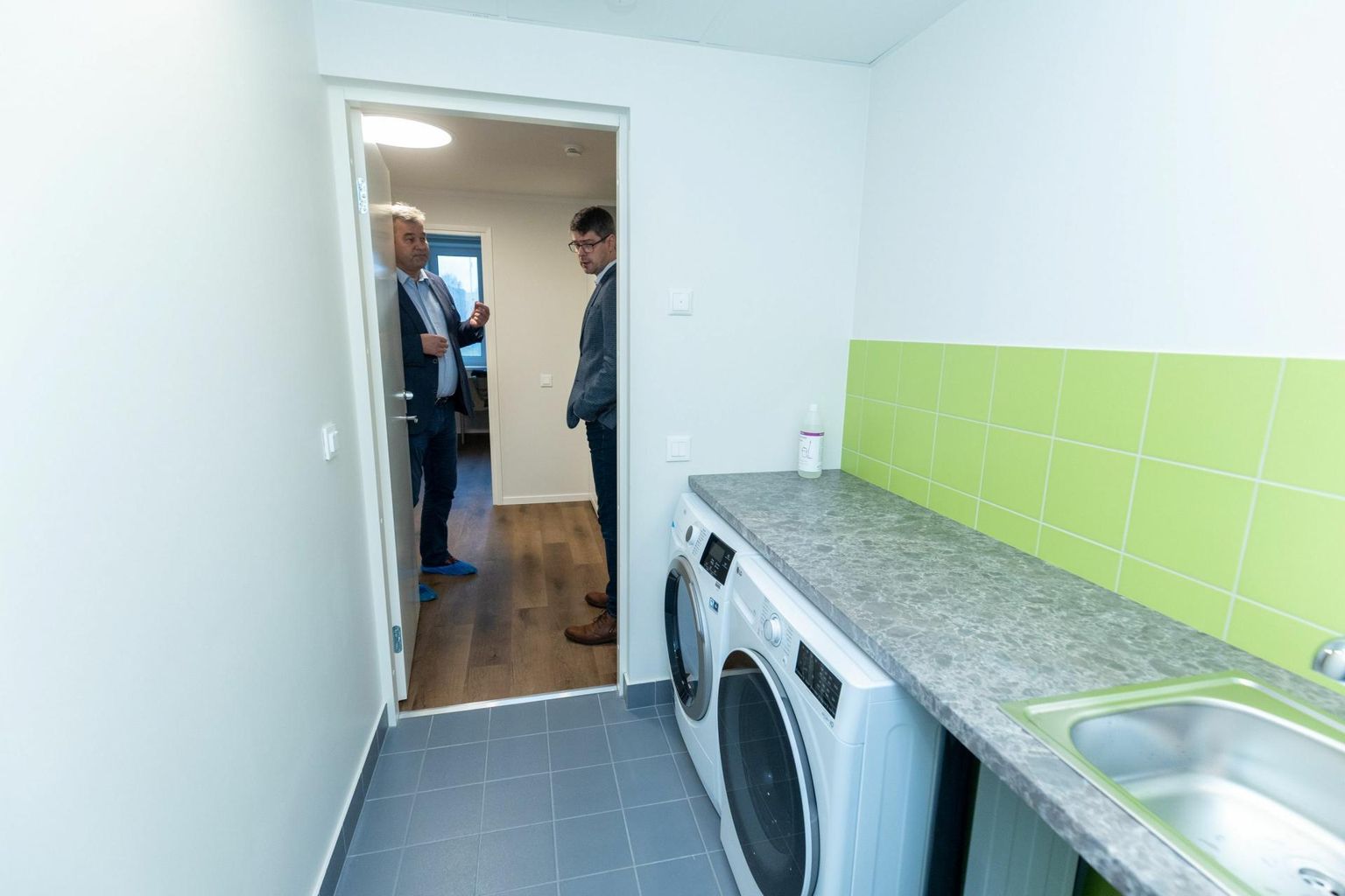 Mihkel Juhkami (vasakul) ja Karl Mänd piiluvad abiruumi, kus erivajadustega inimeste kodu elanikud saavad pesu pesta.