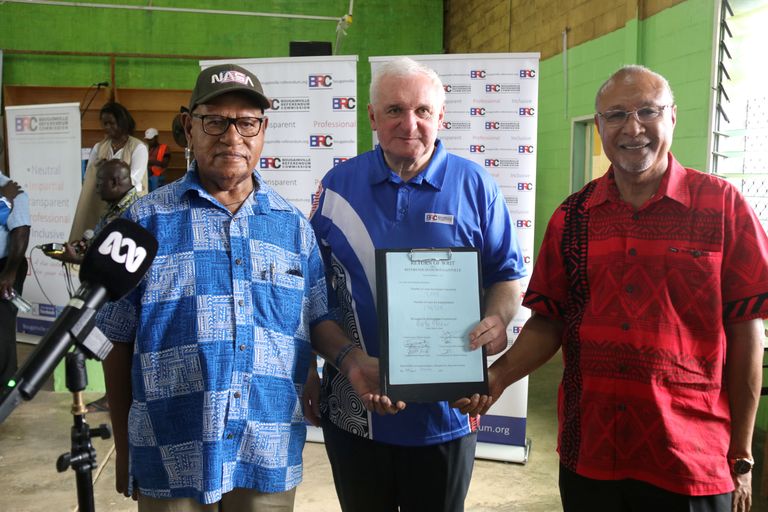 Rahvahääletuskomisjoni juht Bertie Ahern (keskel) hoidmas käes hääletustulemusega dokumenti. Vasakul on Bougainville’i autonoomse piirkonna president John Momis ja paremal on Paapua Uus-Guinea Bougainville’i autonoomse piirkonna eest vastutav minister Puka Temu