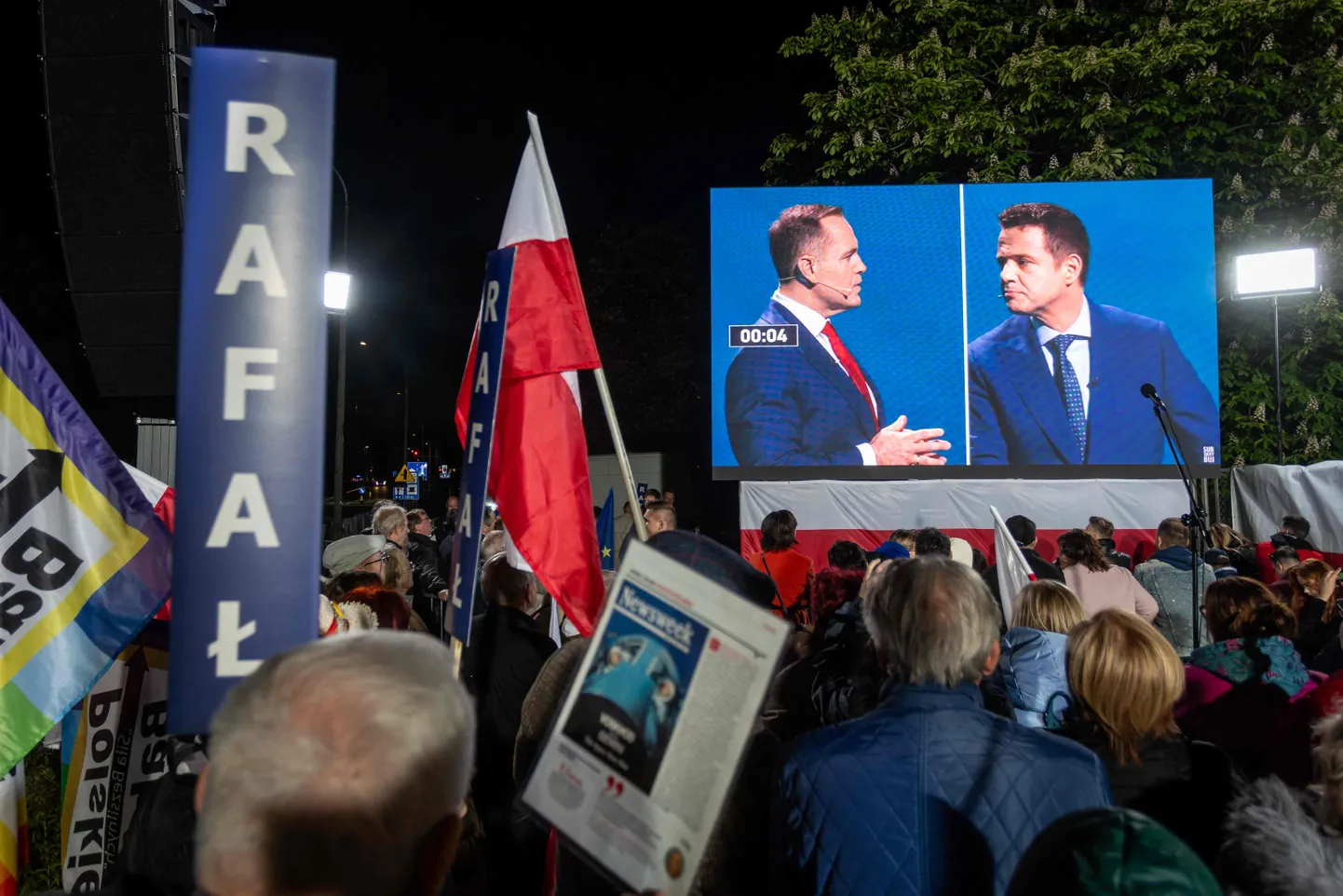 Varšavas mēra un Polijas valdošās Pilsoniskās koalīcijas partijas biedra Rafala Traškovska atbalstītāji vēro savu kandidātu diskusijā ar viņa galveno pretinieku Karol Nawrocki, Polijas labējās partijas "Likums un taisnīgums" (PiS) atbalstīto 2025. gada Polijas prezidenta vēlēšanu kandidātu, prezidenta debašu pārraides laikā uz milzu ekrāna pie Polijas Nacionālās televīzijas galvenās ēkas Varšavā 2025. gada 12. maijā.