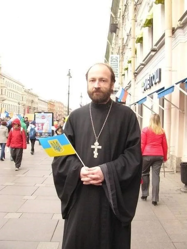 Священник РПЦ Николай Савченко в мае 2014 года на Невском проспекте держит в руках украинский флаг, выражая солидарность с Украиной, на которую уже тогда напала РФ.