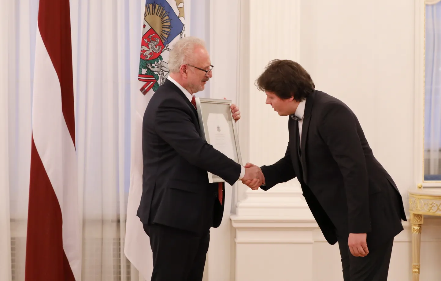Valsts prezidents Egils Levits (no kreisās) pasniedz Cildinājuma rakstu jauniešu kora "Kamēr…" diriģentam Aivim Greteram par trīsreiz iegūto Eiropas kormūzikas balvu "Grand Prix", kļūstot par vienīgo kori pasaulē, kam izdevies šāds sasniegums.