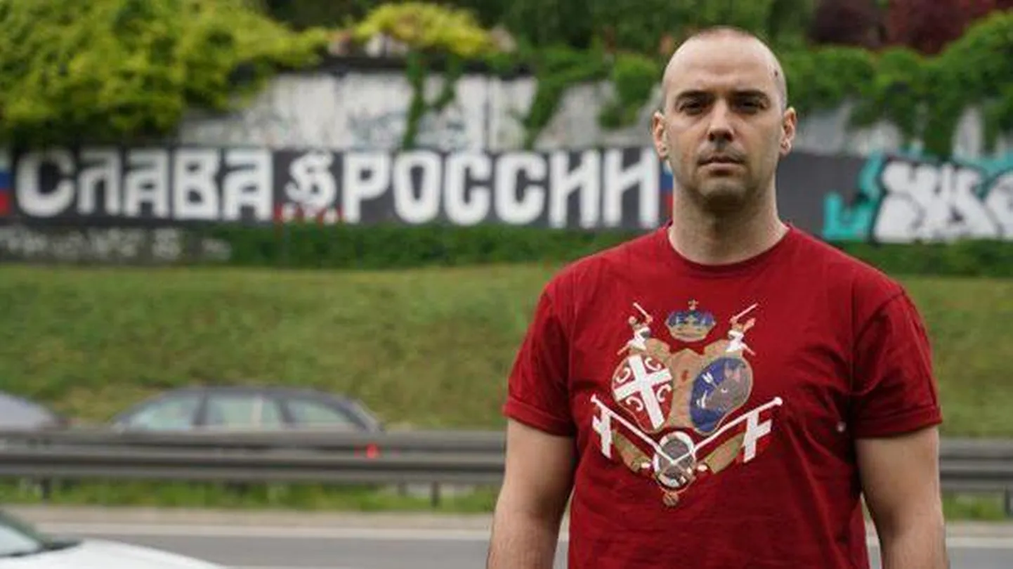 Дамьян Кнежевич стоит перед уличным граффити в Белграде с надписью "Слава России"