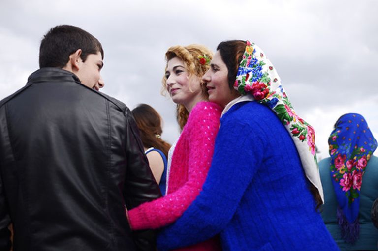 Māte apskāvusi savu meitu, kura sarunājas ar romu jaunieti 