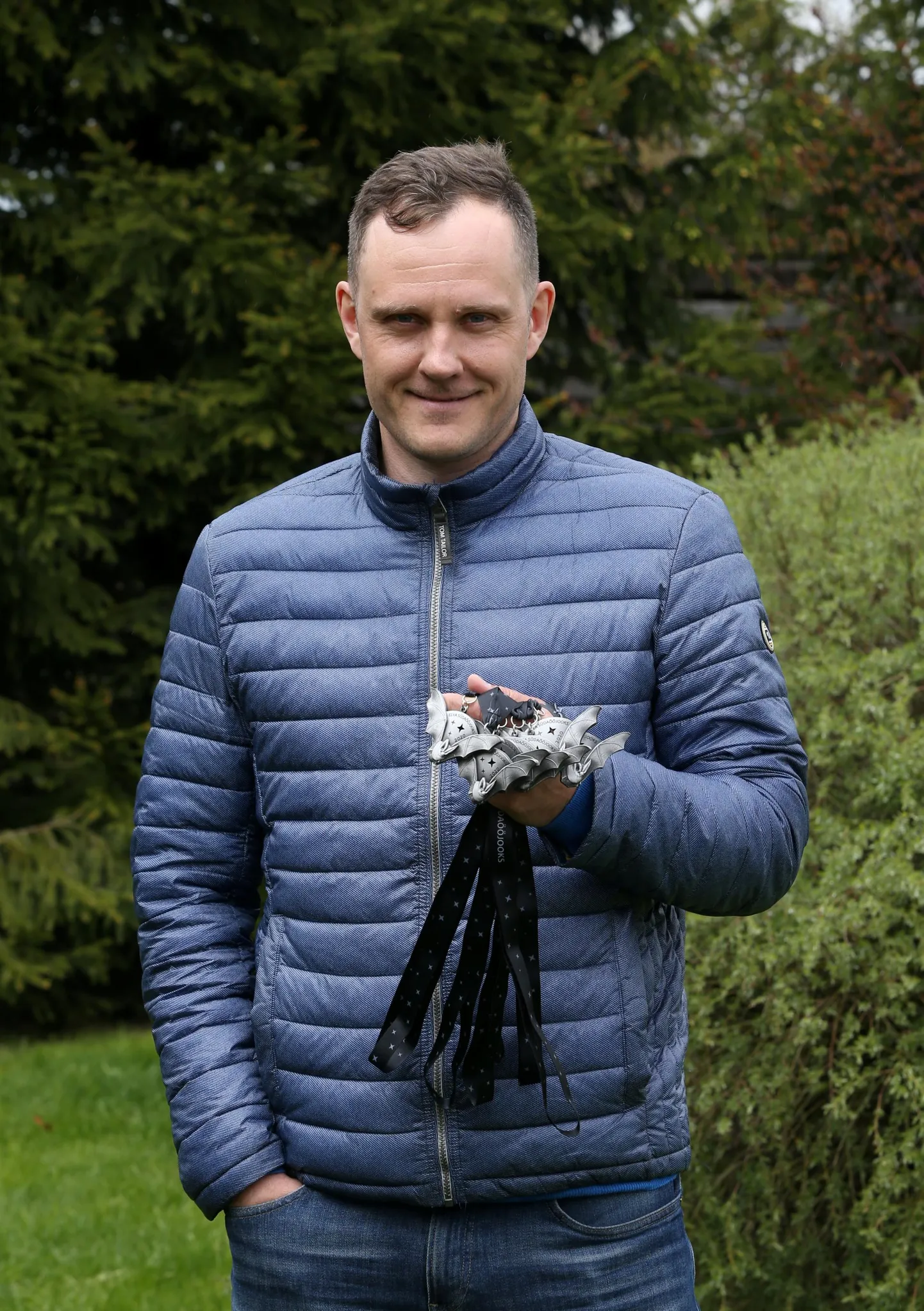 Marek Pihlak hoiab käes nahkhiirt kujutavaid uhiuusi medaleid, mille saavad endale mälestuseks esimesel virtuaalsel Elva südaööjooksul osalejad. ,