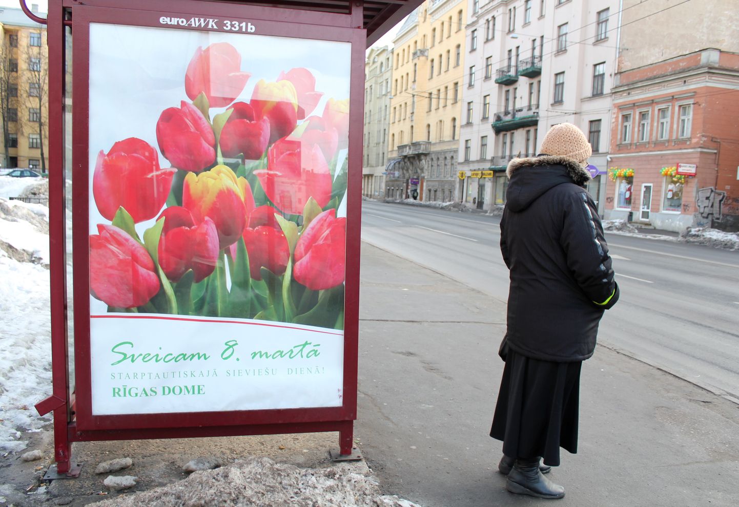 Sieviete pie Rīgas domes apsveikuma plakāta 8. martā, Starptautiskajā sieviešu dienā.