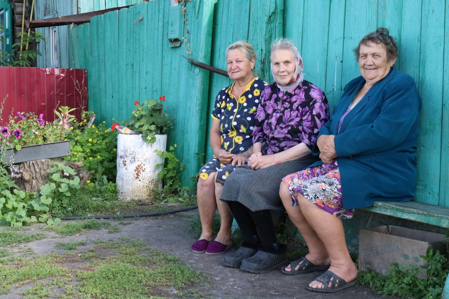 Kovaljovo lõbusad naised (vasakult) Galina Puss, Silvi Rozintseva (Adamson) ja Milvi Petrova (Einbaum) istuvad Milvi tare ees. Kaks abikaasat matnud Milvi elab küla kunagise eesti kooli palkidest ehitatud majas ning peab kasse ja parte.