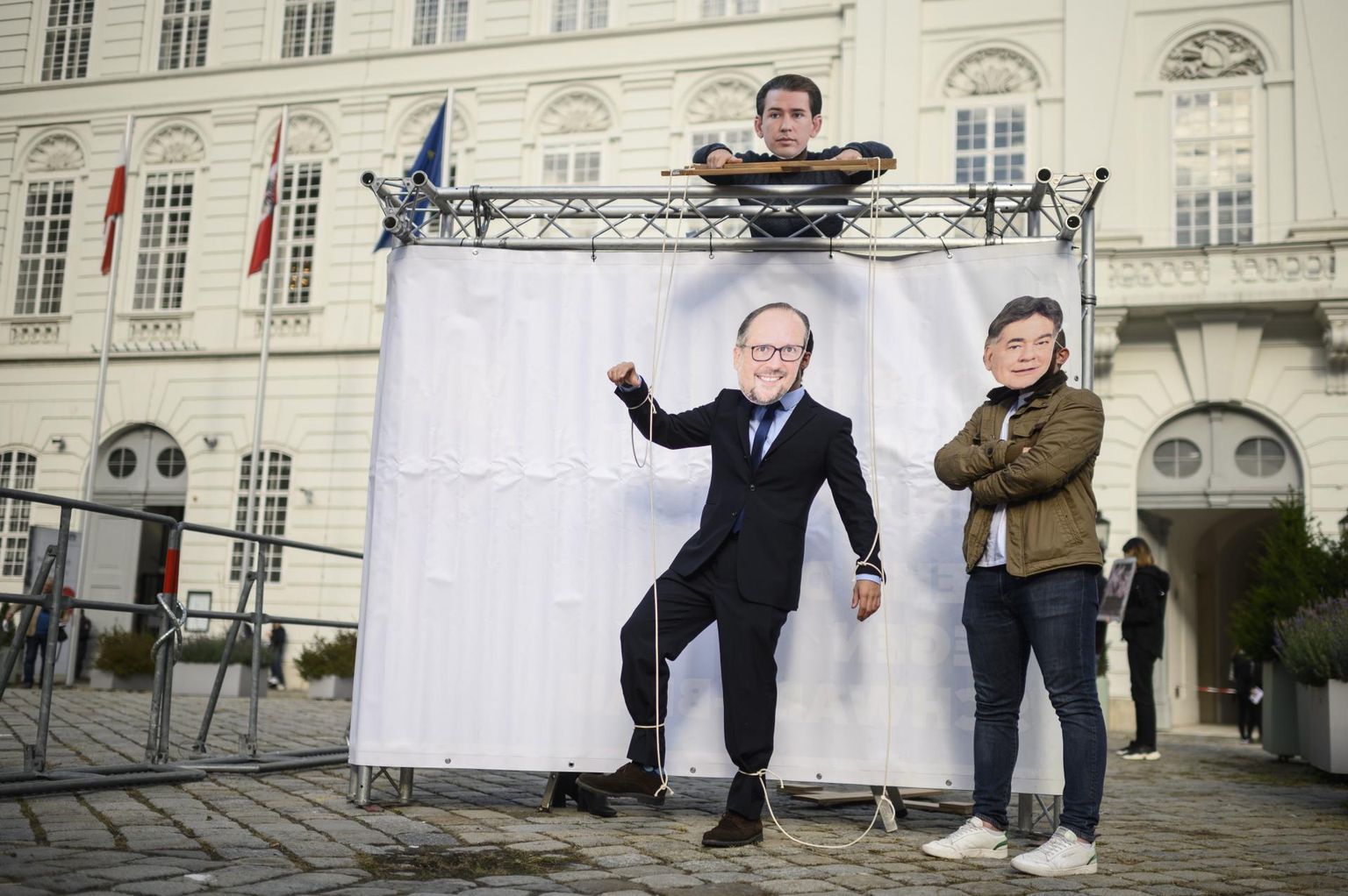 Meeleavaldajad üleeile Viinis parlamendi ajutise tööpaiga Hofburgi palee lähistel maskides, mis kujutavad endist kantslerit Sebastian Kurzi tõmbamas oma ametijärglase Alexander Schallenbergi niite, samas kui Kurzi Rahvapartei valitsuspartneri Roheliste esimees ja asekantsler Werner Kogler vaatab toimuvat pealt.