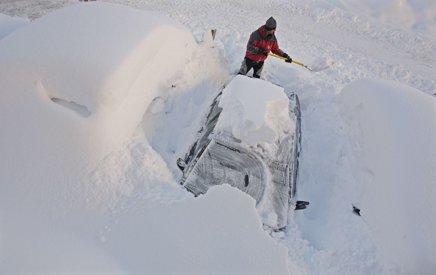 Мужчина в Австрии пытается выкопать из снега свой автомобиль.
