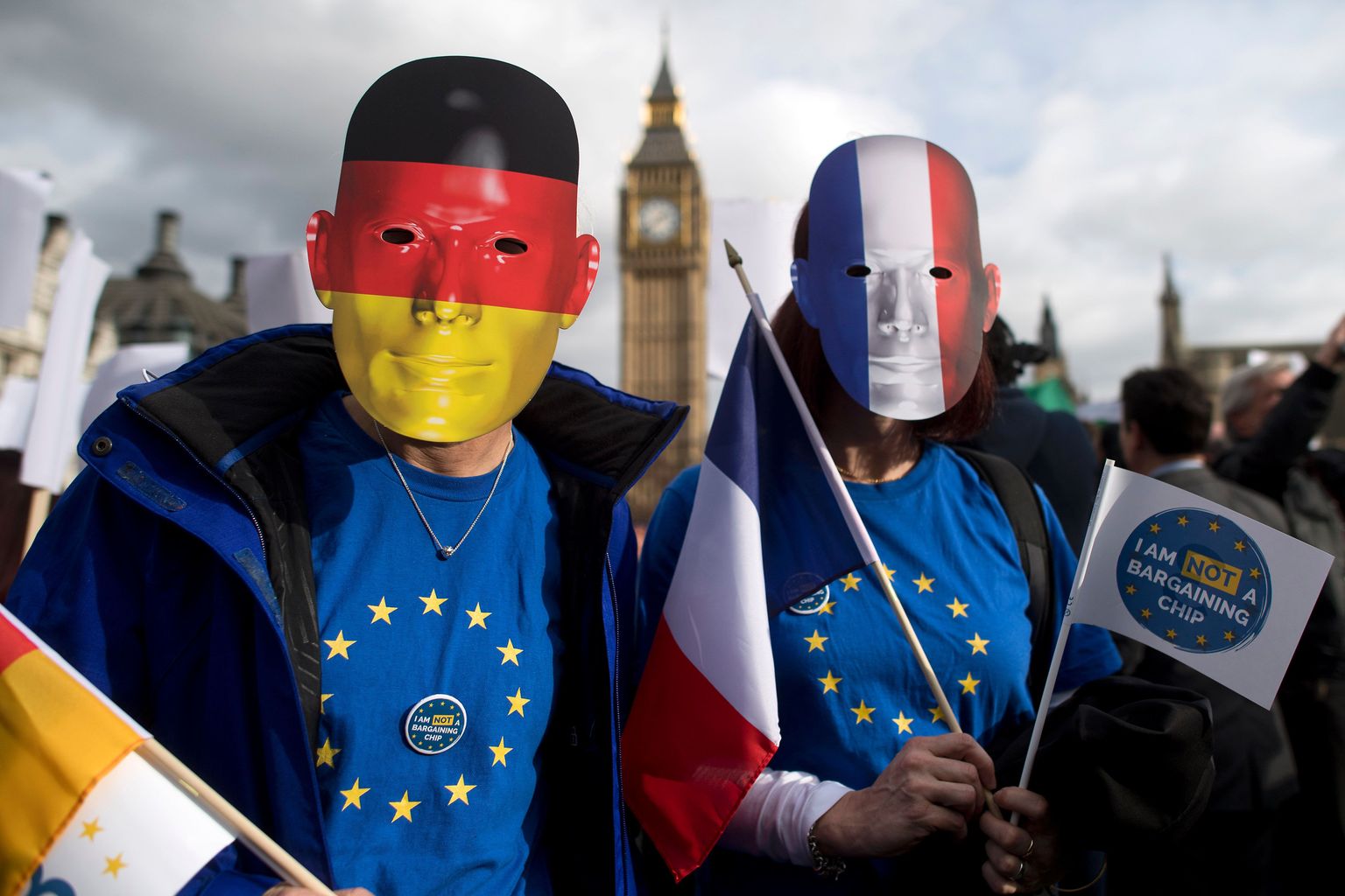 TOPSHOT - Protesters wearing German and French flag face masks pose for a photograph during a "Flag Mob" demonstration in Parliament Square in central London on February 20, 2017, part of a national day of action in support of migrants in the UK. 
Under the banner