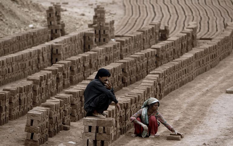 Pakistani mees istub müüril ja teeb suitsu, kui tema naine teeb tellisetehases tööd. Foto: AP