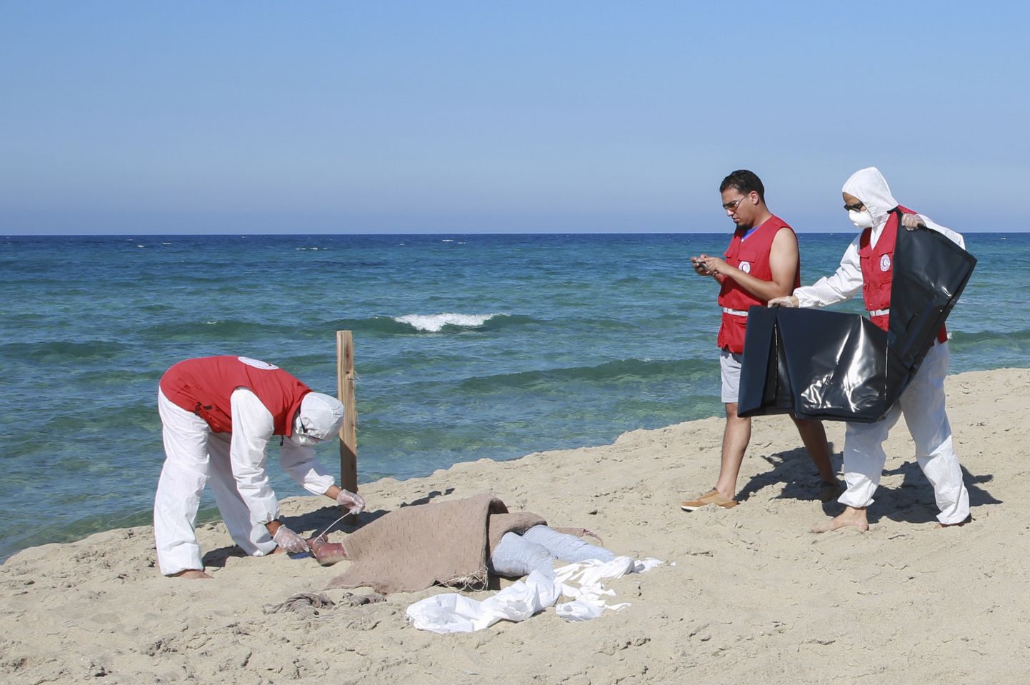 Liibüa Punase Poolkuu töötajad riigi rannikul Khomsi linna juures Vahemeres uppunud migranid surnukeha juures.