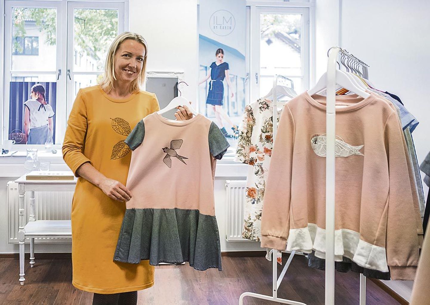 ILM by Karin kaubamärgi looja Karin Sülluste hoiab käes kleiti, millel oleva tikandi autor on peretuttava laps.