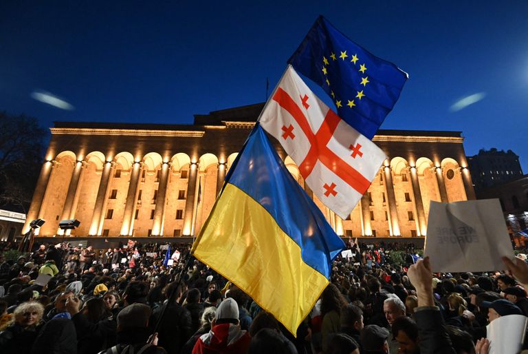 Протестующие в Тбилиси около парламента Грузии машут флагами Грузии, Украины и ЕС, скрепленными вместе, 8 марта 2023 года.