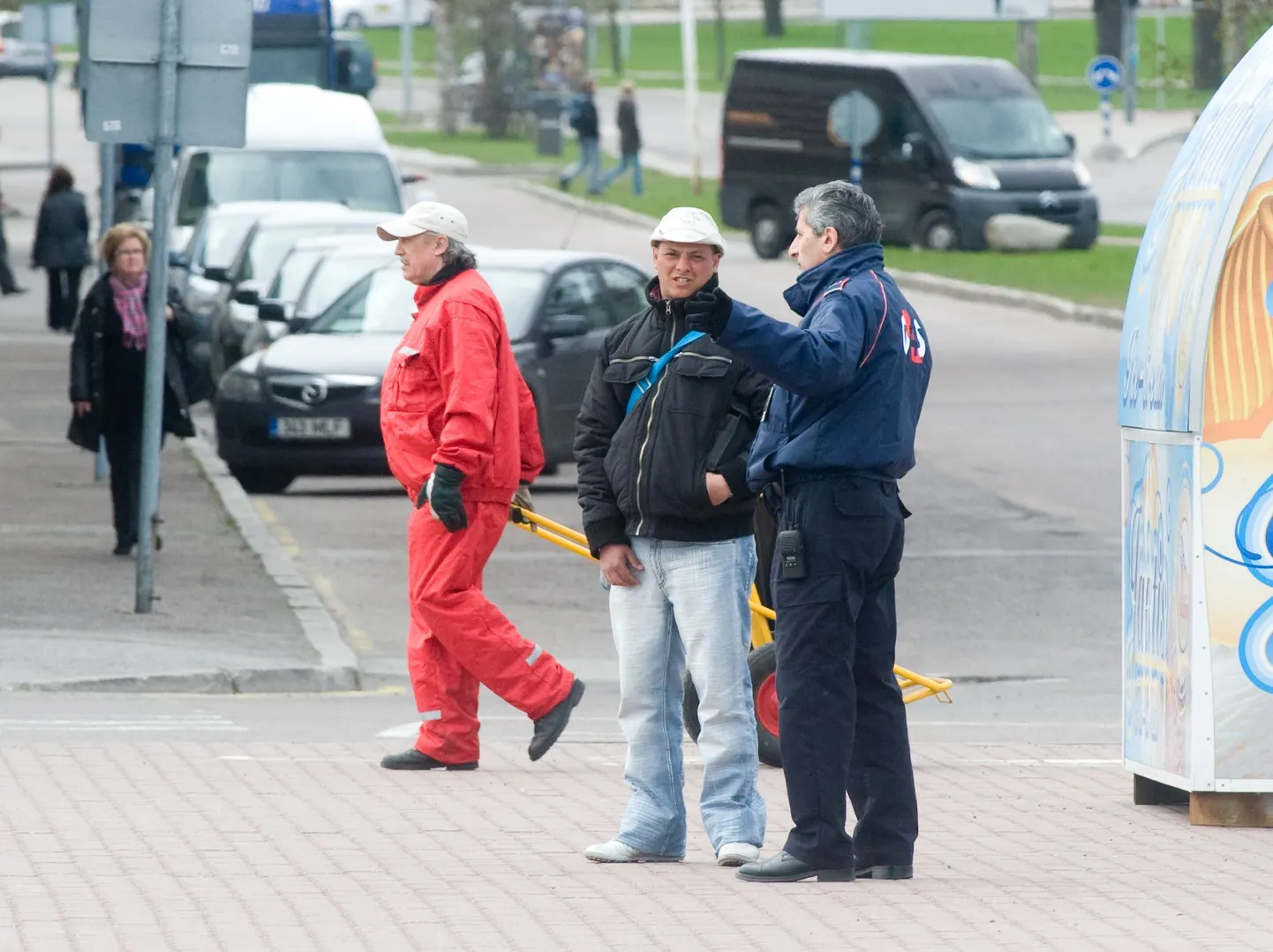 Turvatöötaja tõrjub pealetükkivat binoklimüüjat sadama ees busside parklas.
