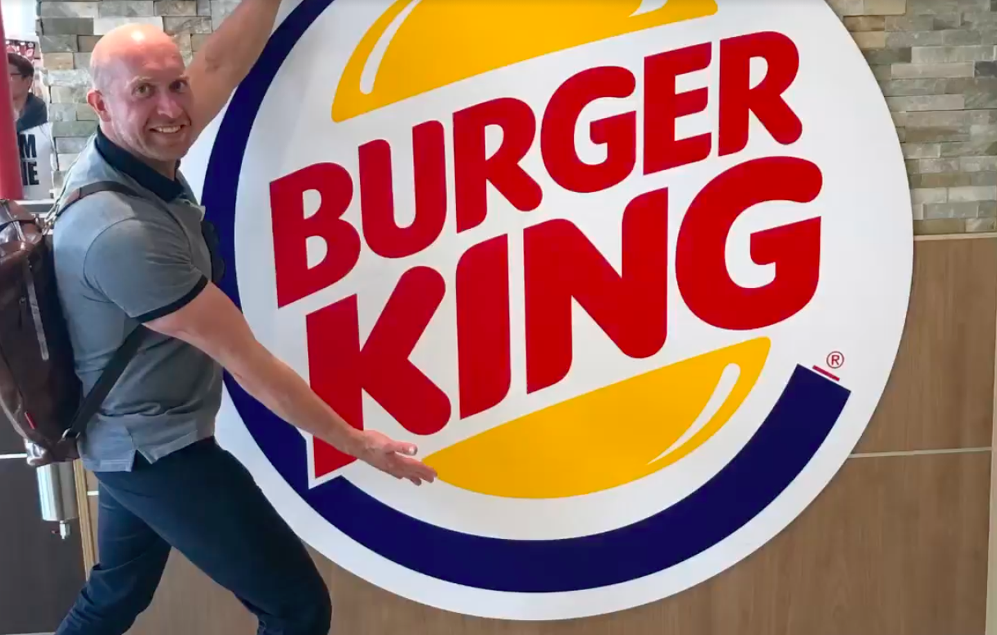 Erik Orgu Burger King kiirtoidurestorani logo kõrval poseerimas.