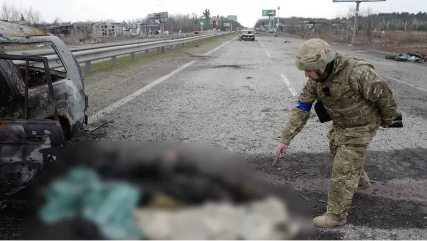 Украинский военный показывает на обгоревшие человеческие останки у сгоревшего автомобиля