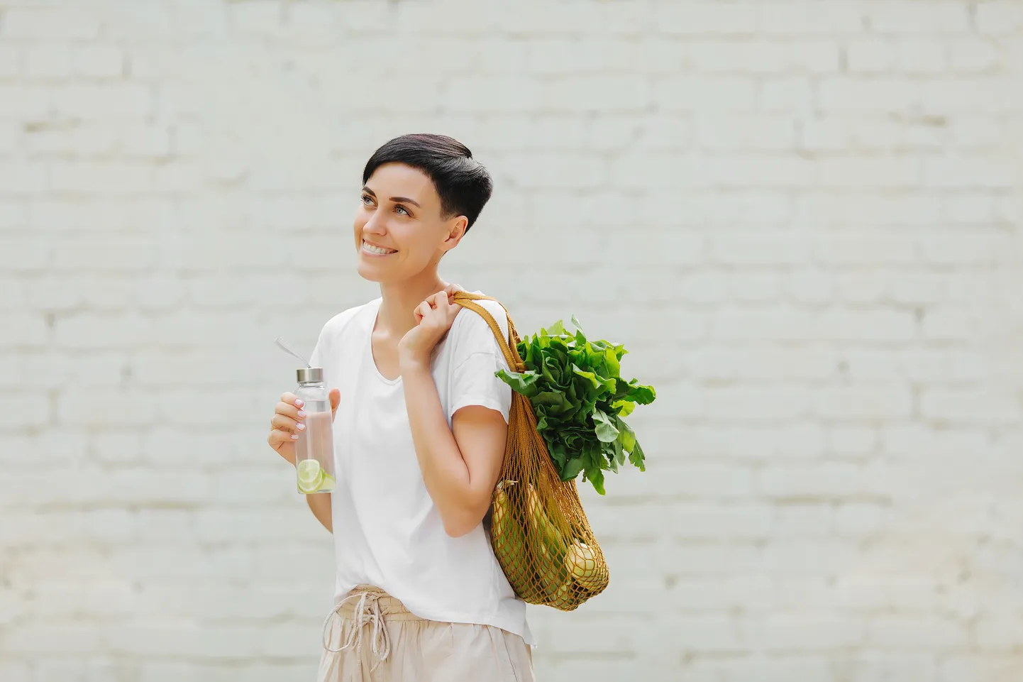 Young woman in light summer clothes with a eco bag of vegetables, greens and reusable water bottle.  Sustainable lifestyle. Eco friendly concept.