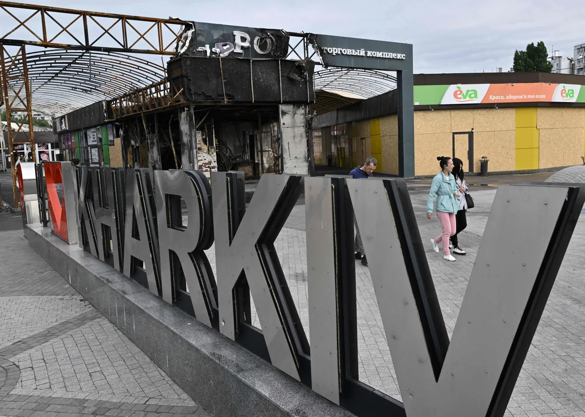 People walk past an installation reading "I love Kharkiv" next to a damaged market in the Saltivka district, northern Kharkiv on May 29, 2022.