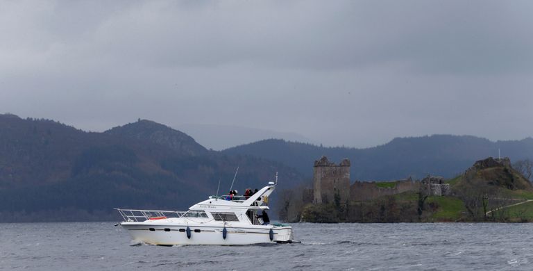Turistid kaatriga Loch Nessi järvel, kaugemal on näha Urquharti kindlust