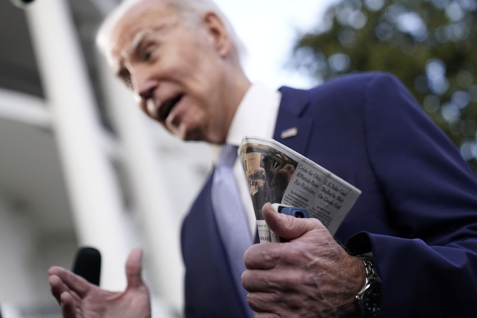 Kahe telefoni ja ajalehega Joe Biden enne kopterile astumist ajakirjanike ees.