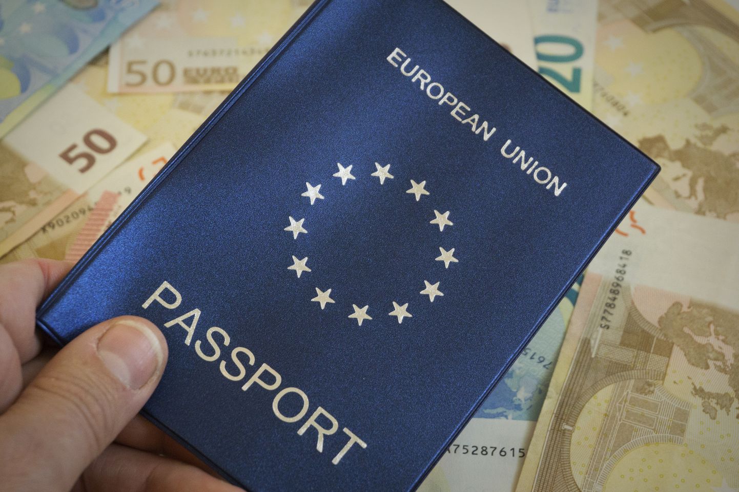 Shallow depth of field shot of man an holding European Union passport against backdrop of euro notes