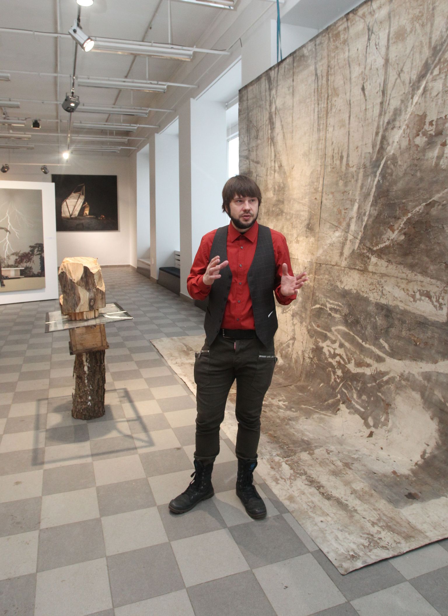 Läti kunstiakadeemia maaliosakonna juhataja professor Andris Vītoliņš tutvustas näitust bituumeni järele lõhnava hiiglasliku installatsiooni «9 + 13 = 15» juures. Selle autor on Raitis Hrolovičs.
