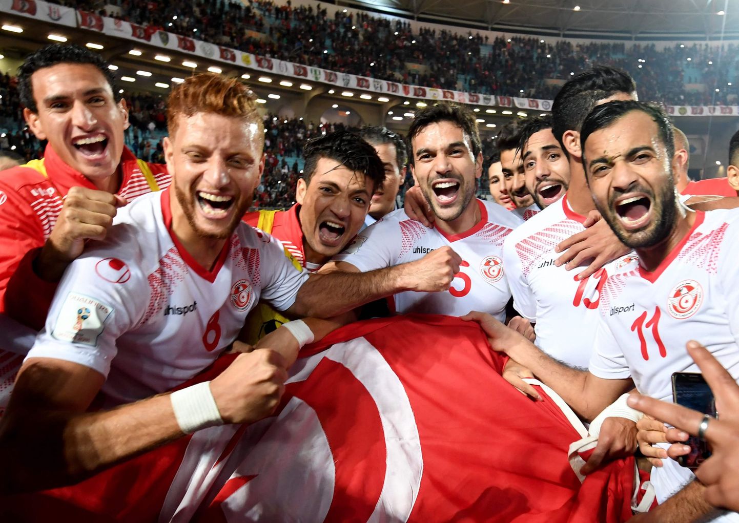 Players of the Tunisian national football team celebrate with their national flag after qualifying for the 2018 World Cup finals after winning their qualifiers match against Libya at the Rades Olympic Stadium in the capital Tunis on November 11, 2017. / AFP PHOTO / FETHI BELAID